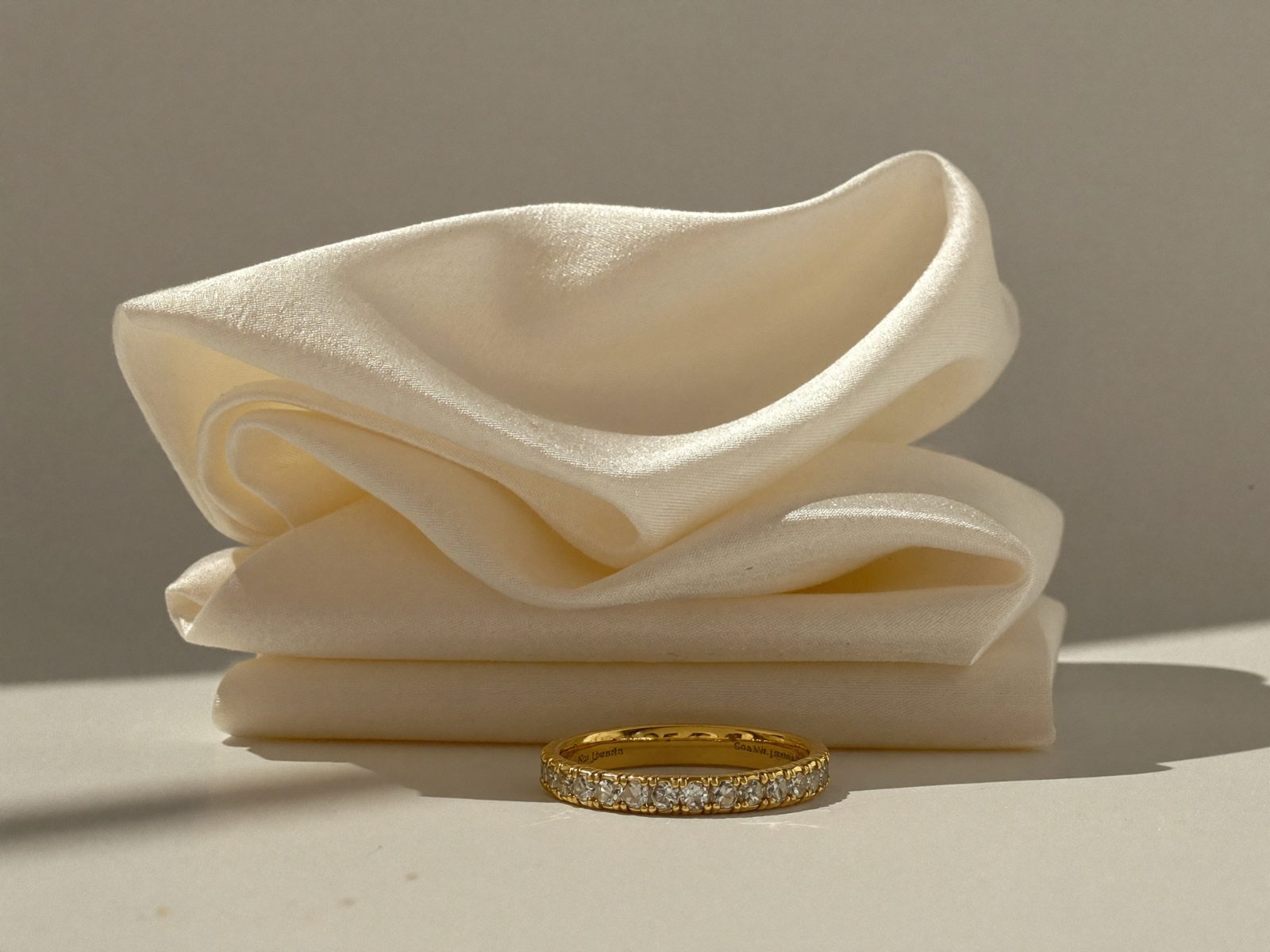 A gold diamond eternity band standing against folded cream silk